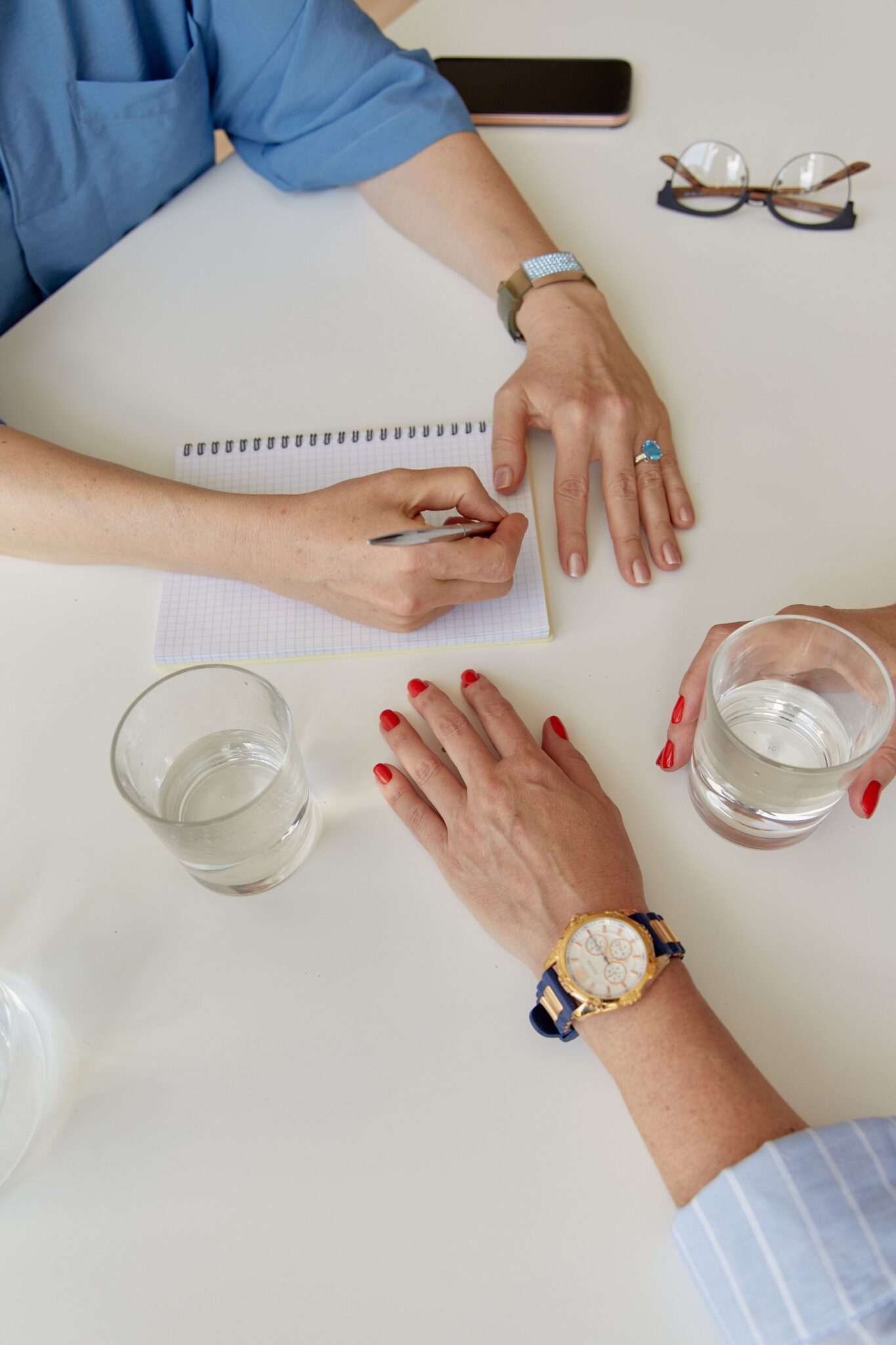 Hands of professionals collaborating, taking notes, and drinking water at an office meeting.